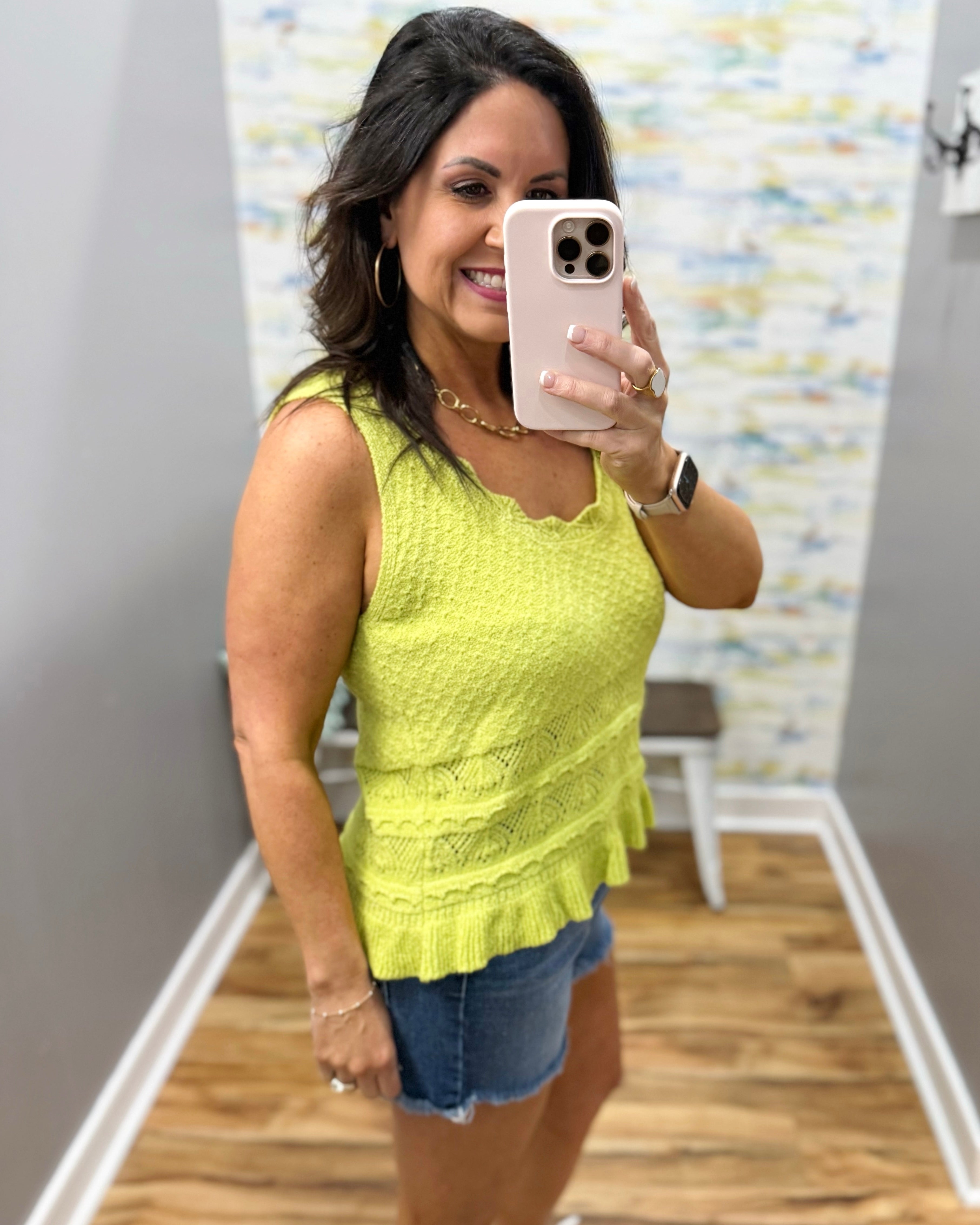 Woman taking a mirror selfie wearing a yellow lace top and denim shorts.