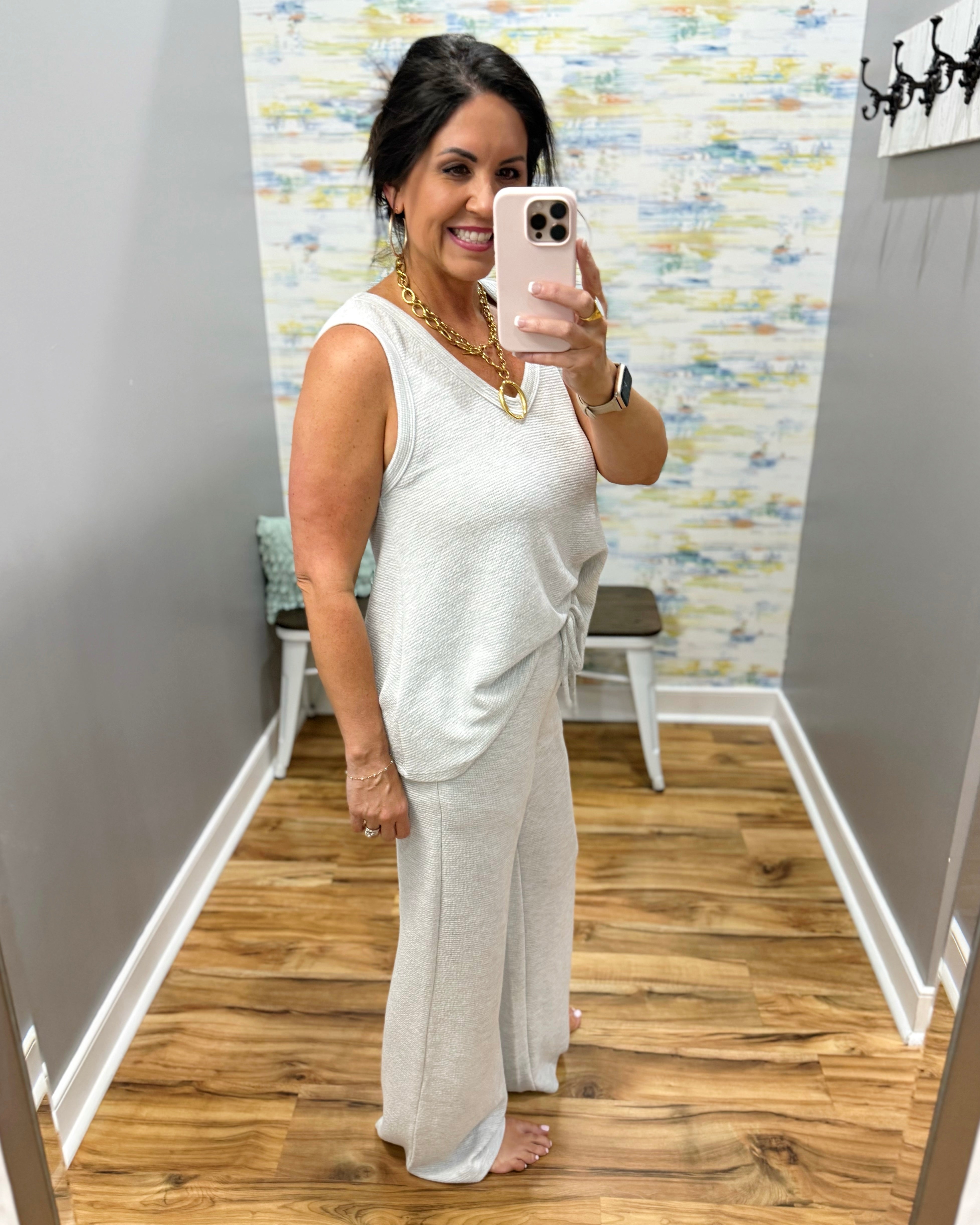Woman taking a mirror selfie wearing a white outfit in a room with wooden flooring and a colorful wall.