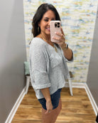 Woman taking a mirror selfie wearing a gray sweater and denim shorts in a room with a colorful wall.
