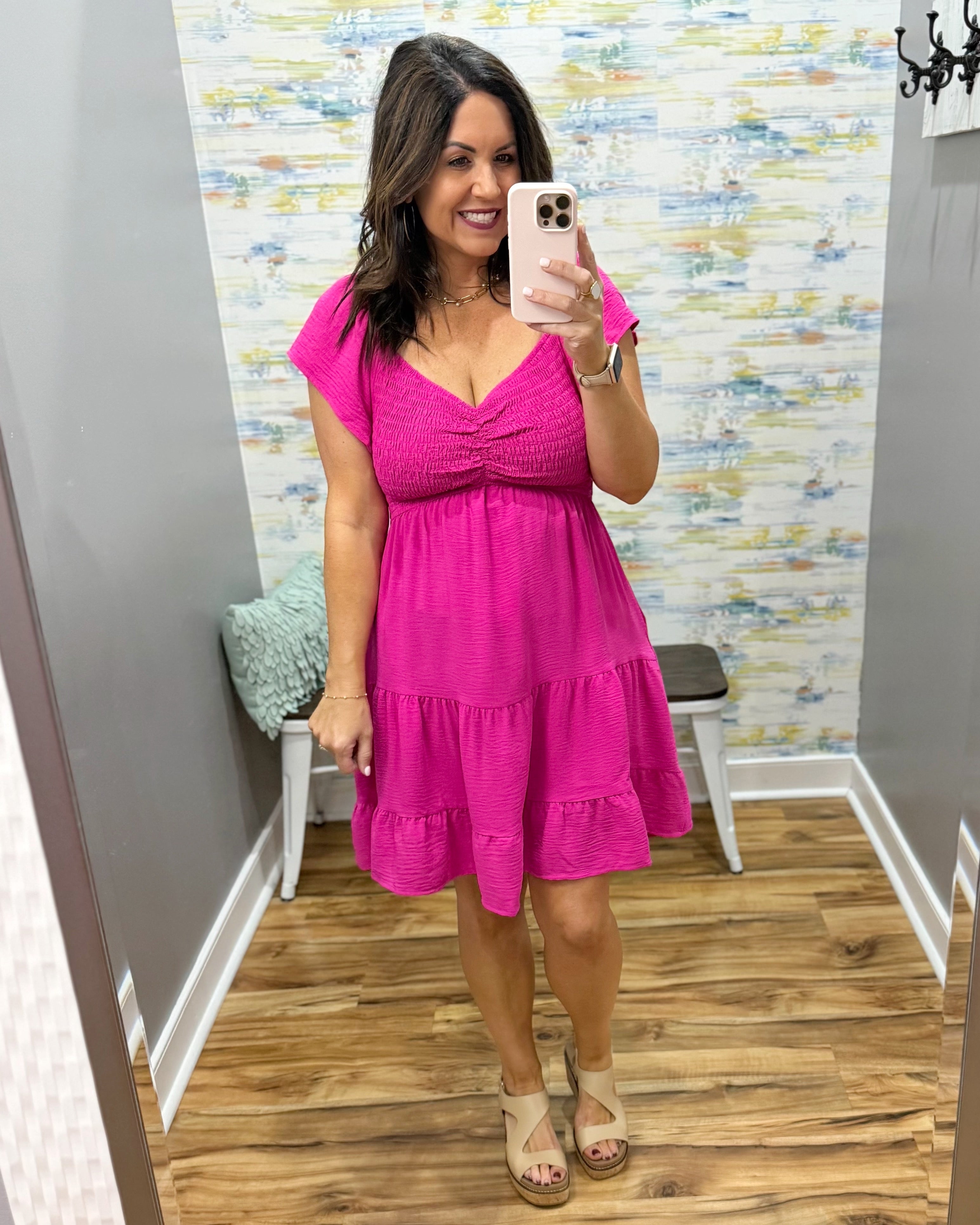 Woman taking a mirror selfie wearing a pink dress in a room with a colorful wall.