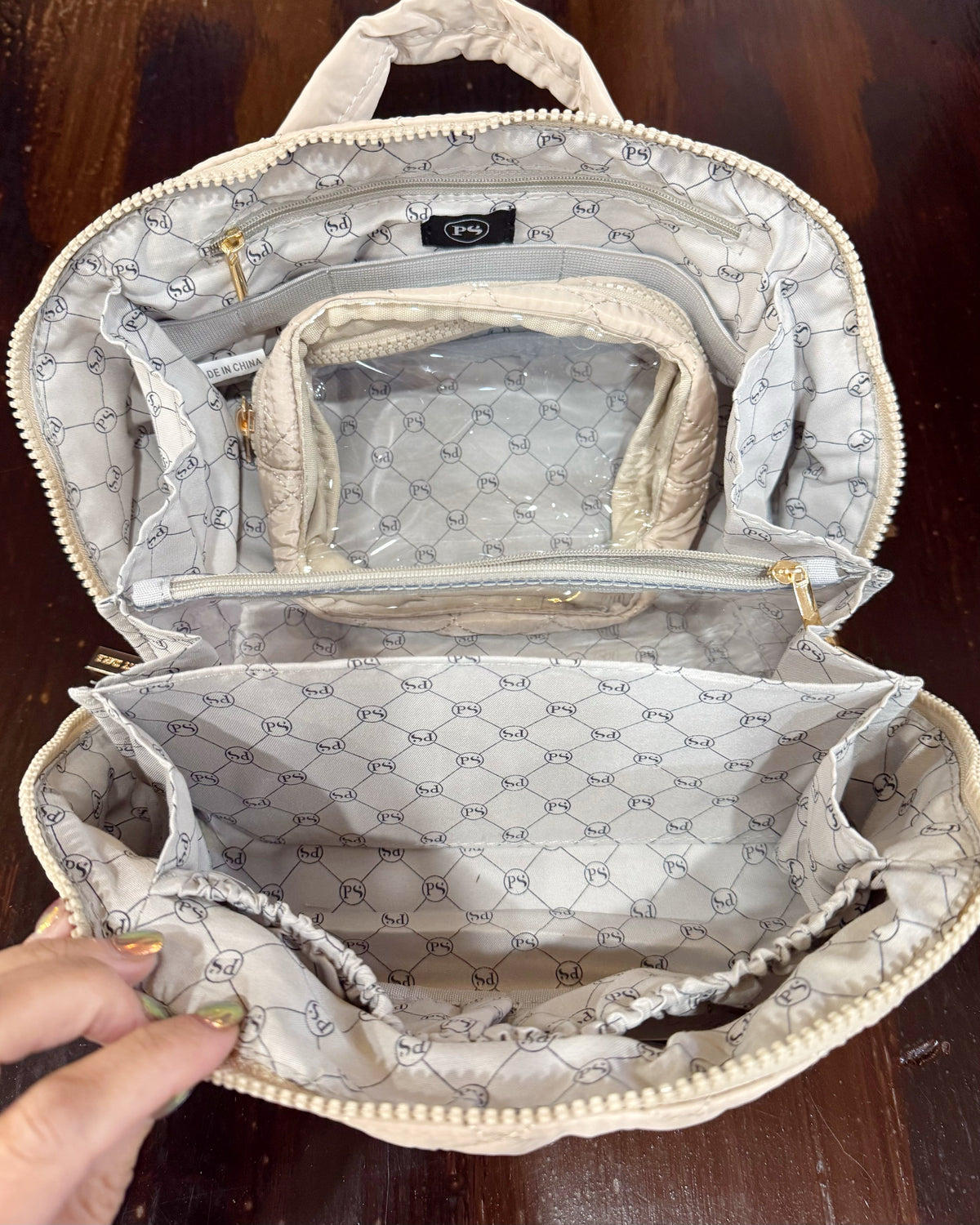 An open taupe color patterned organizer bag with multiple interior compartments, shown on a dark wooden surface.