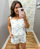 woman wearing a white top with blue palm trees embroidered on it.