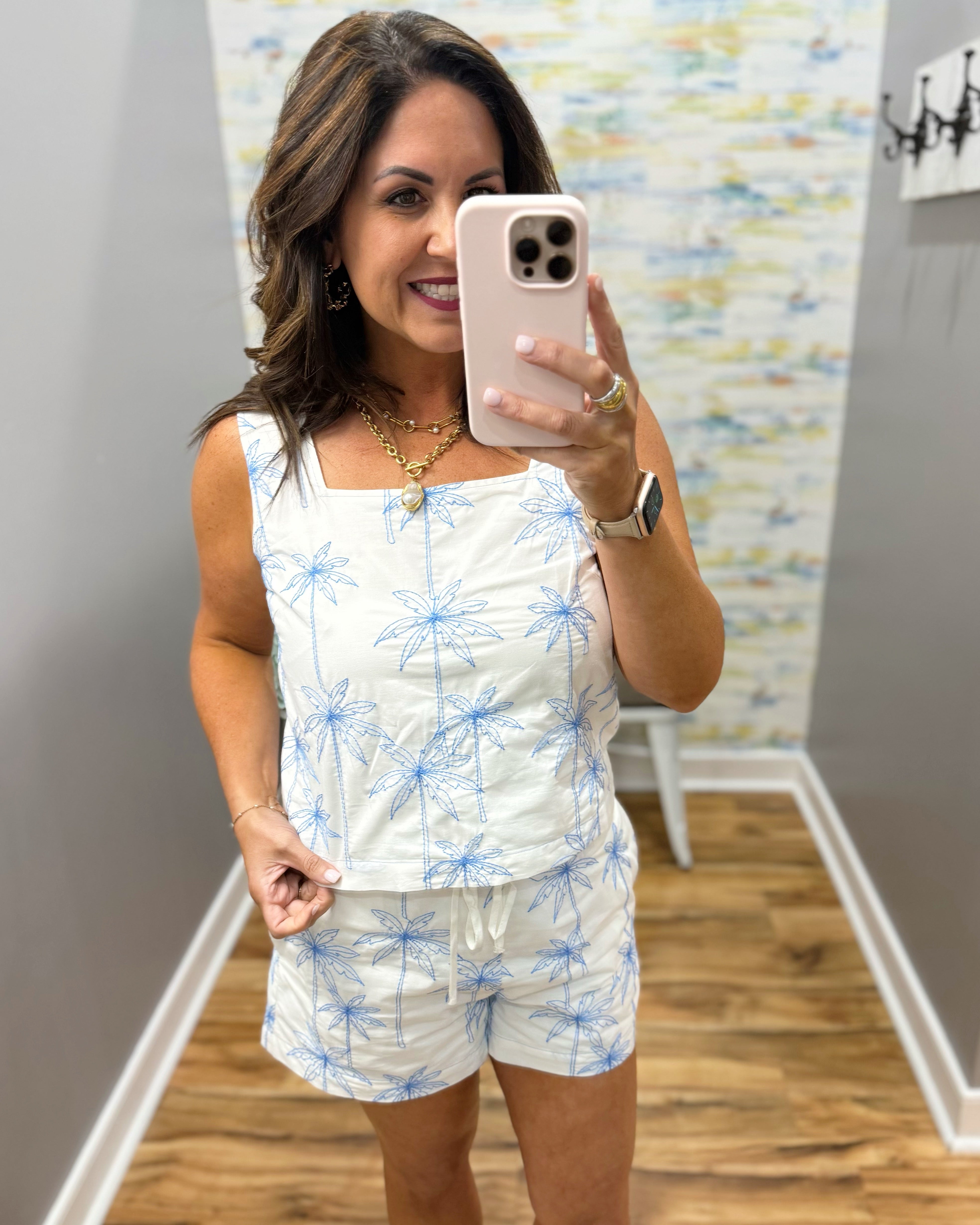 woman wearing a white top with blue palm trees embroidered on it.
