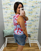 Woman taking a mirror selfie wearing a floral top and denim shorts in a room with colorful wall art.