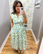 Woman taking a mirror selfie wearing a floral dress in a room with patterned wallpaper.