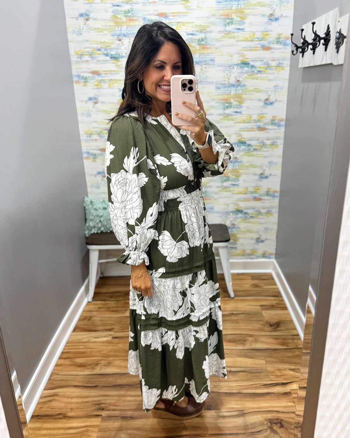 A woman takes a mirror selfie wearing a long-sleeve olive green maxi dress with a white floral print. The dress features a V-neckline, smock waist.