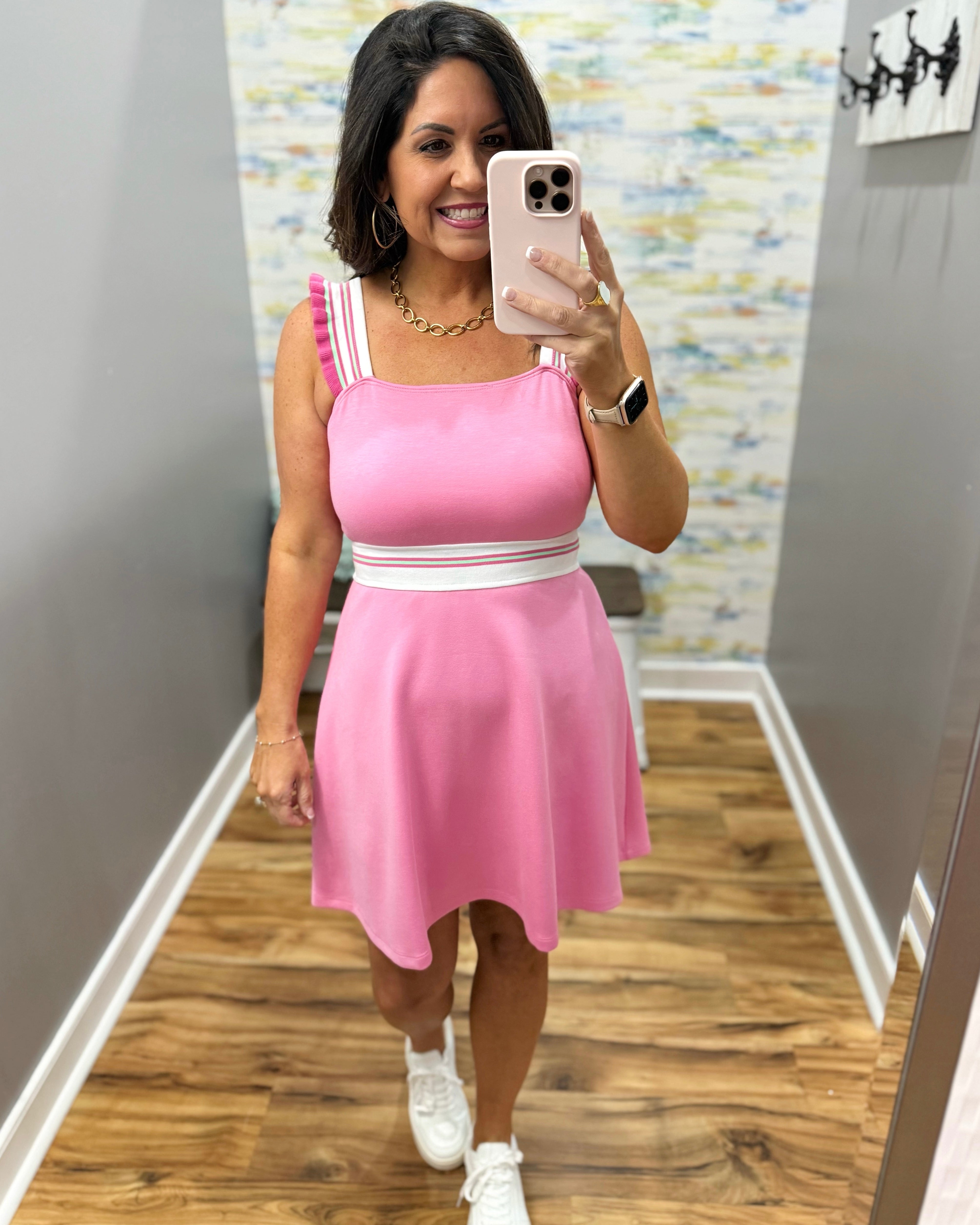 Woman taking a mirror selfie wearing a pink dress with white accents.