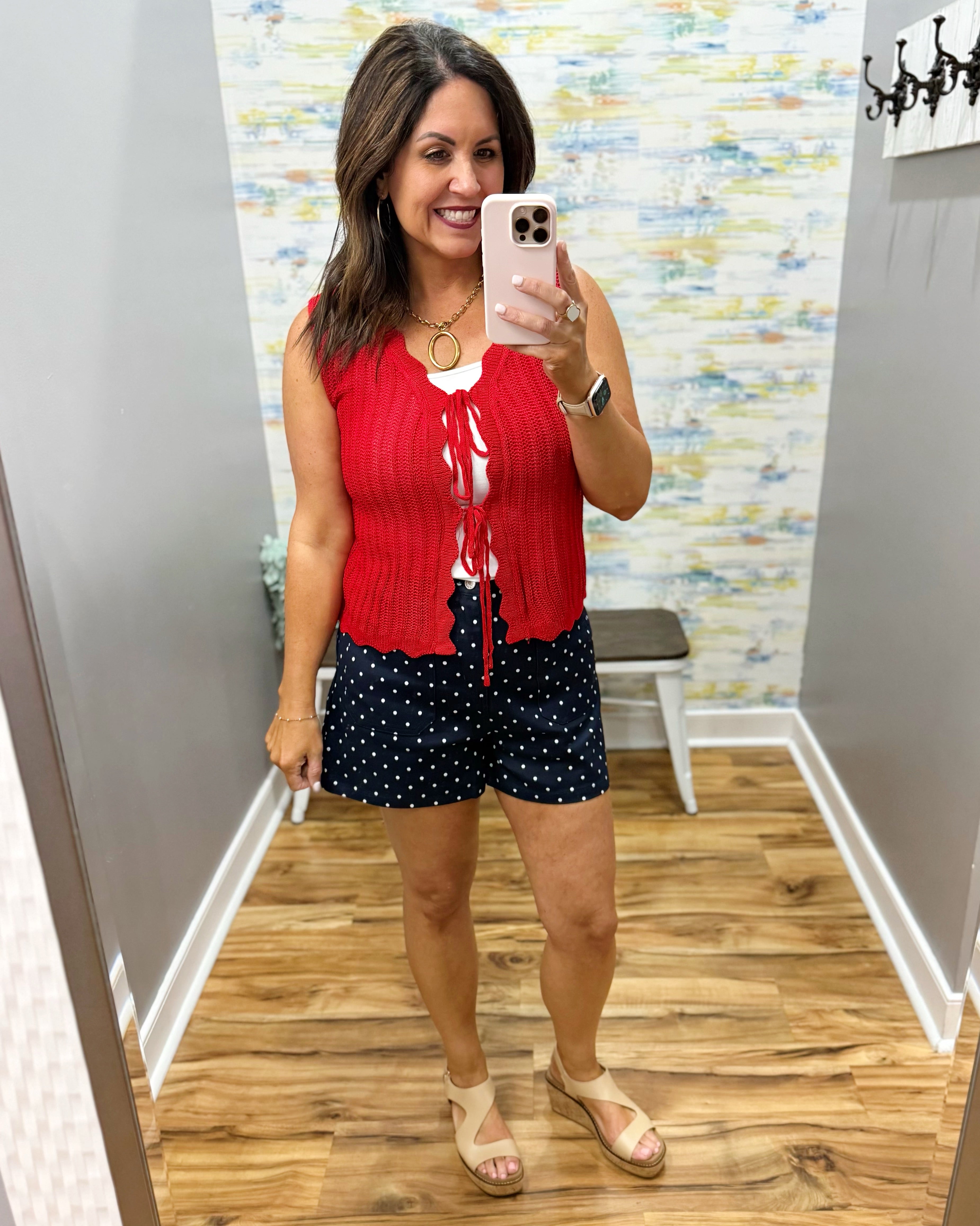 Woman taking a mirror selfie wearing a red sleeveless top and navy shorts with white polka dots.