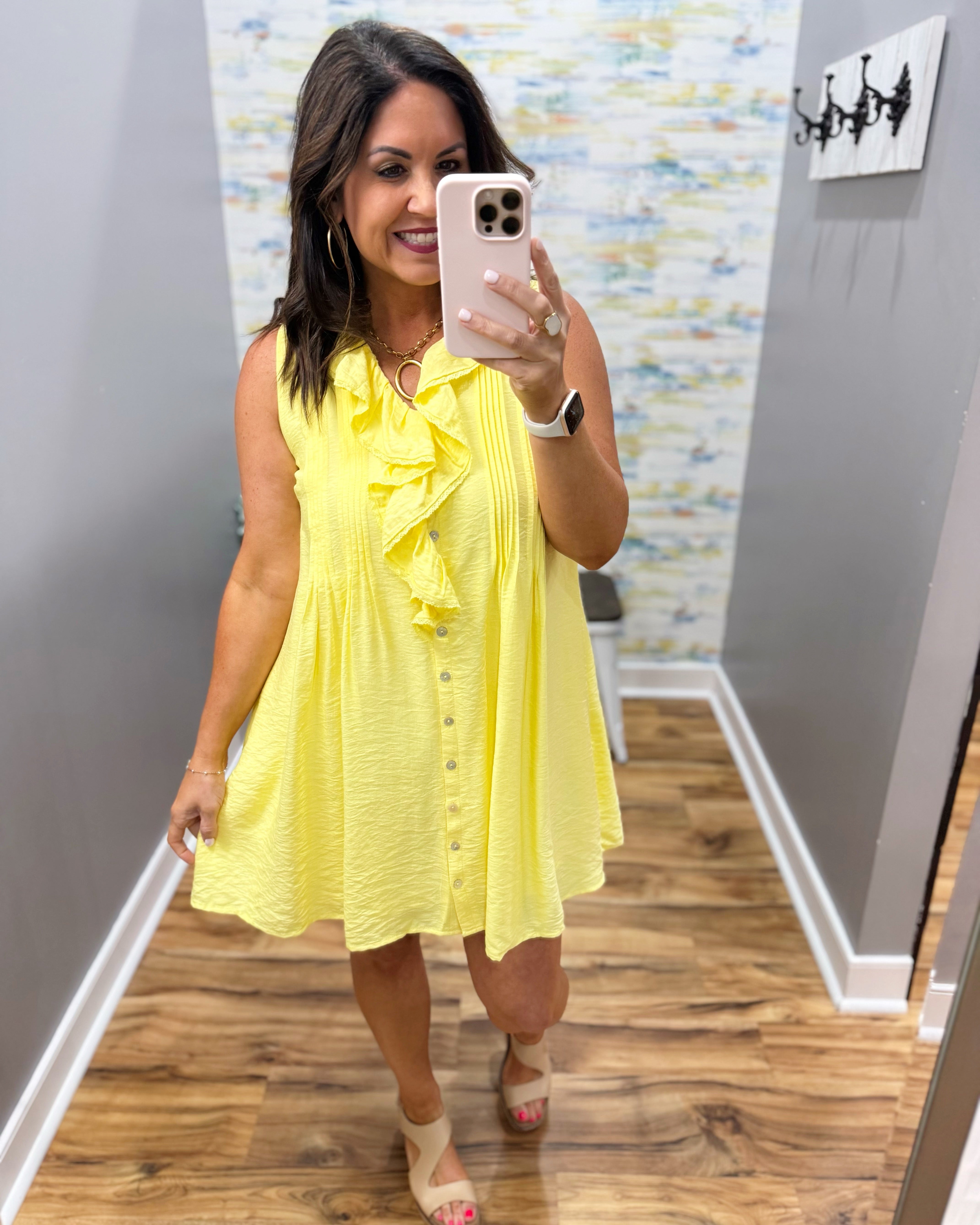 Woman taking a mirror selfie wearing a yellow dress in a room with a colorful wall.