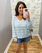 Woman wearing a light blue striped sweater and denim shorts.