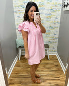 Woman taking a mirror selfie wearing a pink and white striped dress in a room with a colorful wall.