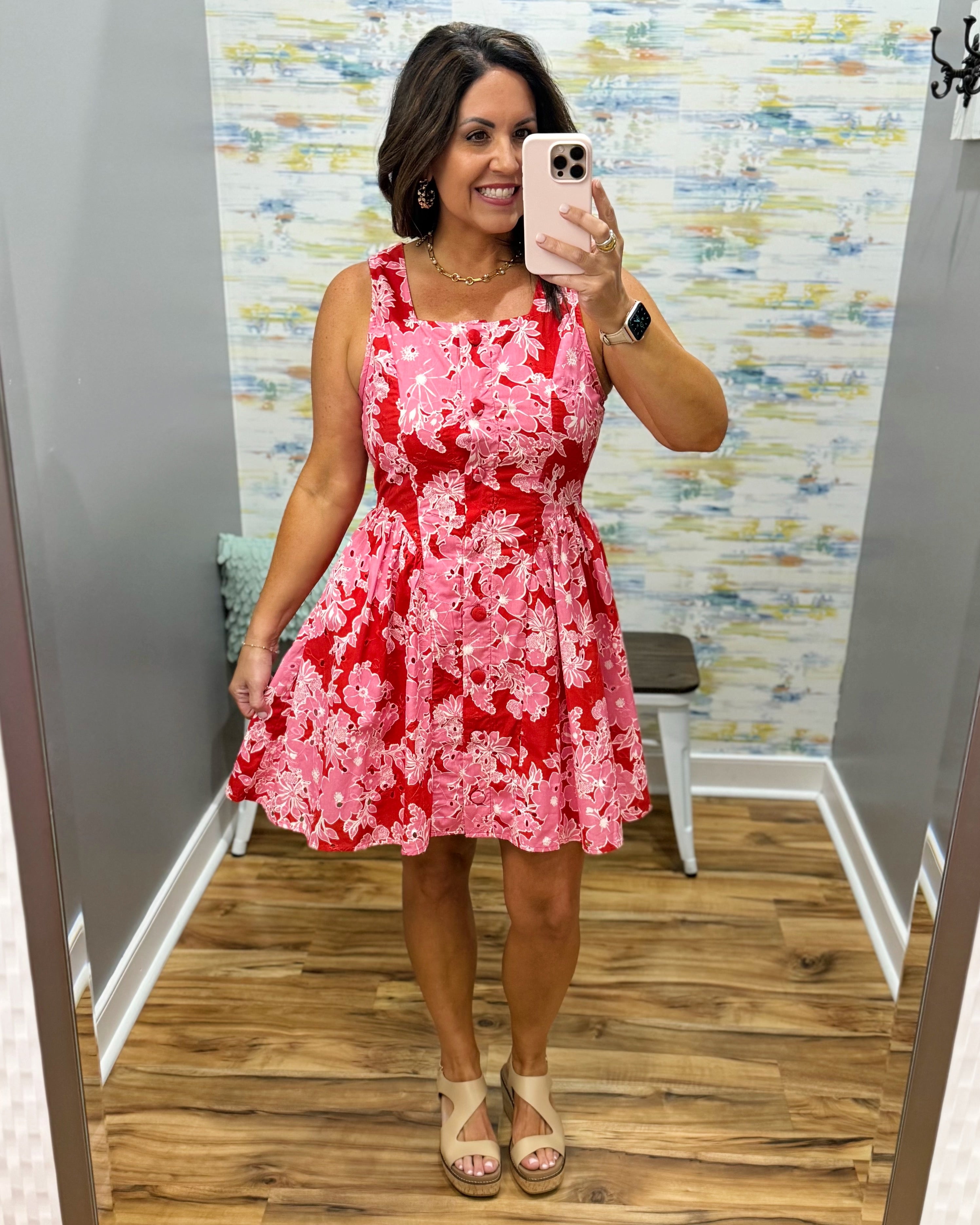 Woman taking a mirror selfie wearing a red floral dress in a room with patterned wallpaper.