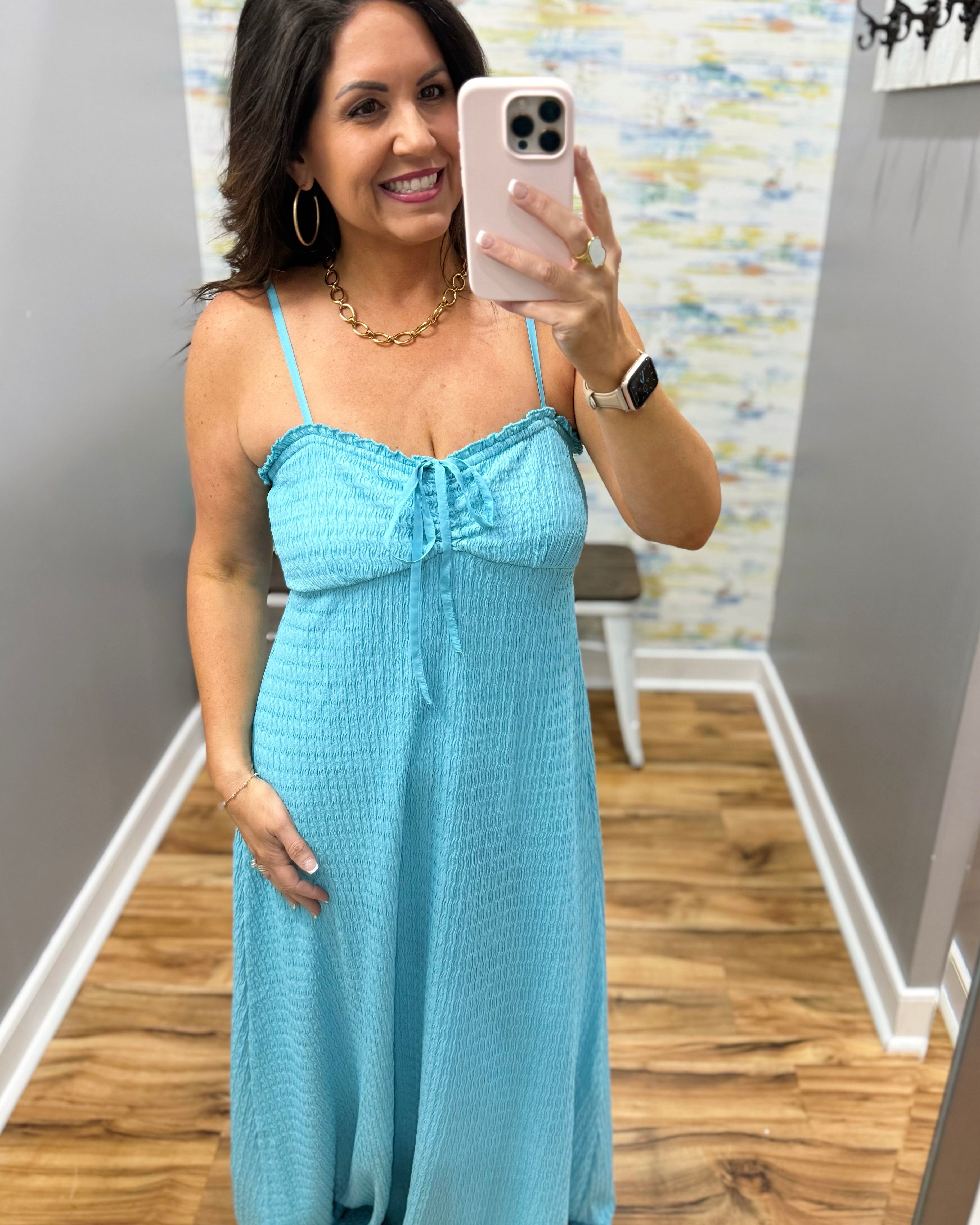 Woman taking a mirror selfie wearing a light blue dress in a room with a patterned wall.