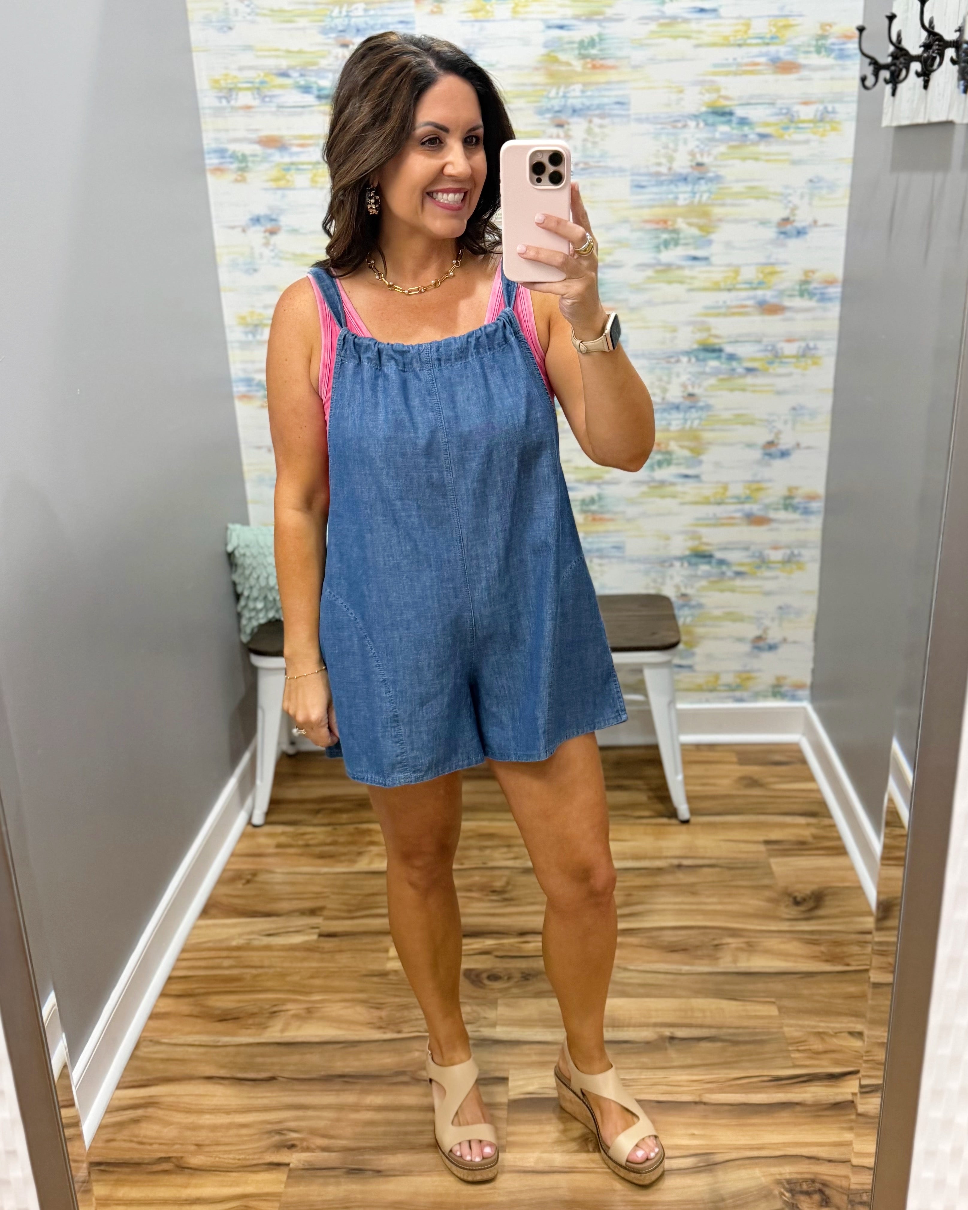 Woman taking a mirror selfie wearing a blue dress in a fitting room.
