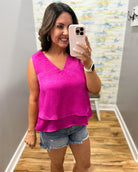 Woman taking a mirror selfie wearing a bright pink top and denim shorts in a room with a patterned wall.