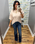 A woman takes a mirror selfie in a fitting room wearing a light beige short-sleeve knit sweater and dark blue flare jeans.