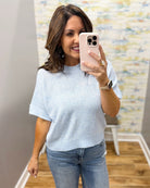 Woman taking a mirror selfie wearing a light blue top and jeans in a room with a colorful wall.