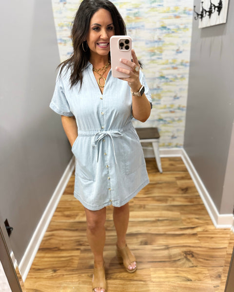 Woman wearing a light blue dress in a room with wooden flooring and a colorful wall.