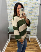 A woman takes a mirror selfie wearing a chunky knit sweater with wide horizontal stripes in dark green and cream, paired with blue jeans.