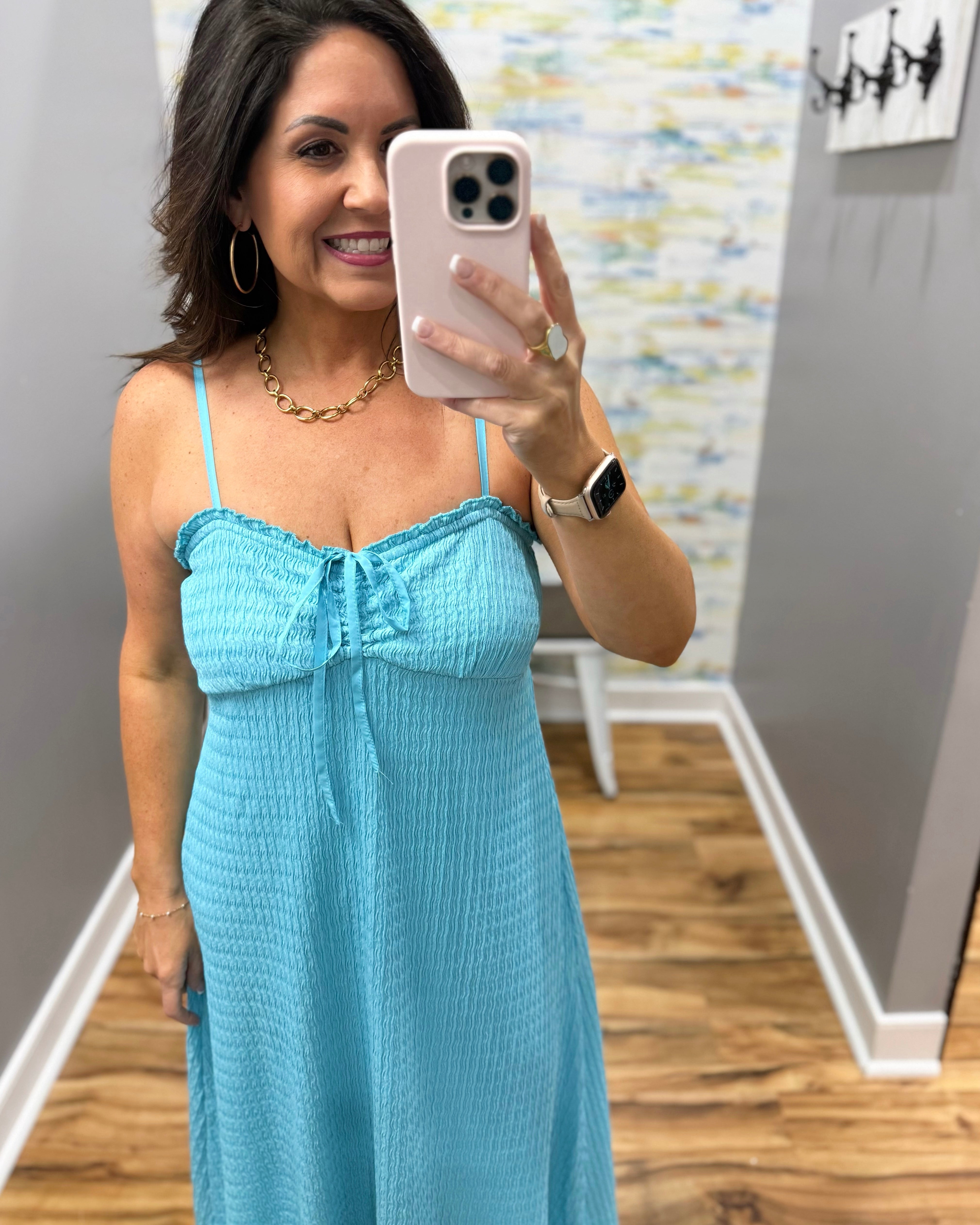 Woman taking a mirror selfie wearing a blue dress in a room with a colorful wall.