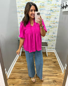 Woman taking a mirror selfie wearing a bright pink top and blue jeans in a room with a patterned wall.