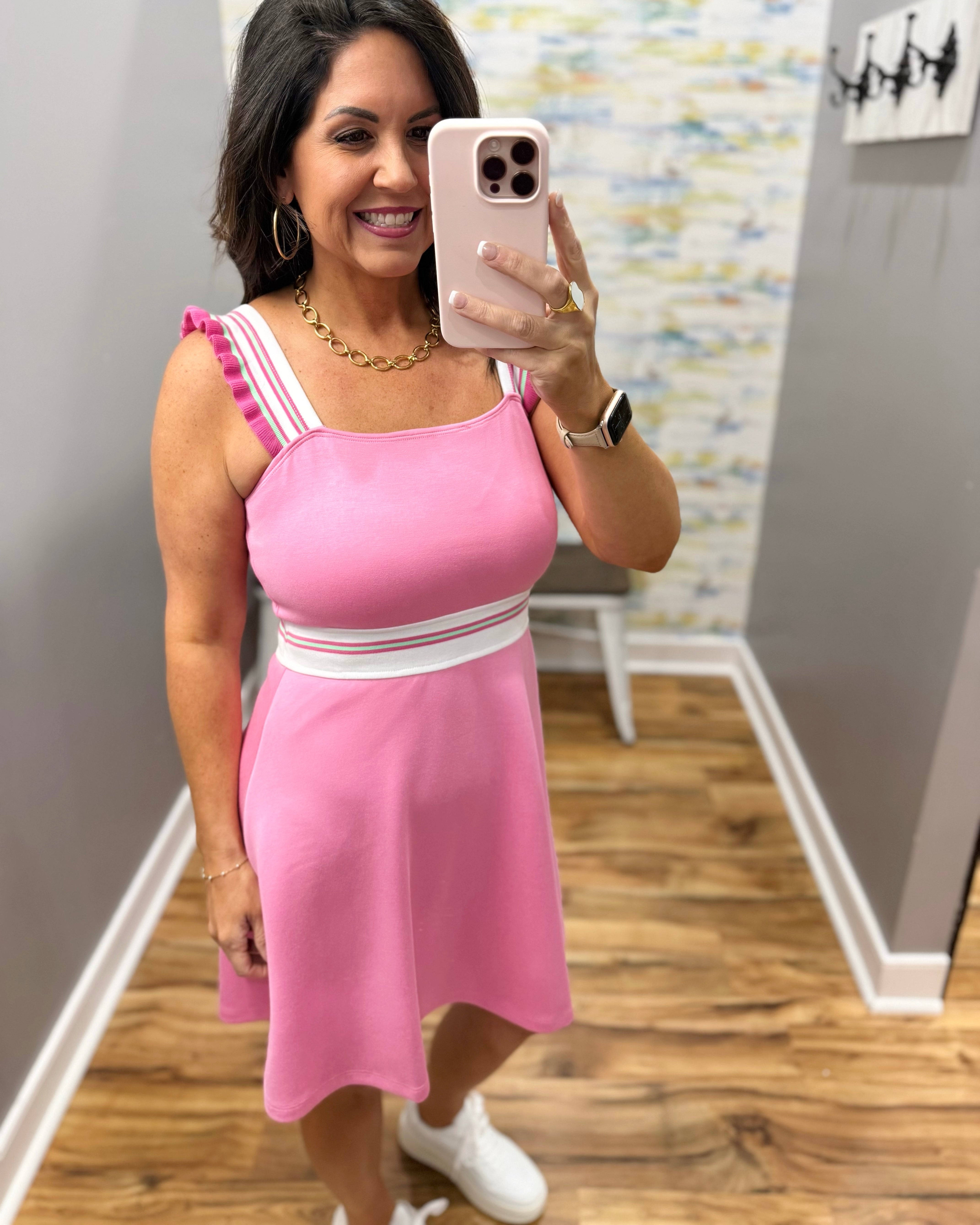 Woman taking a mirror selfie wearing a pink dress with white straps in a room.