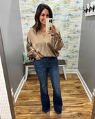 A woman takes a mirror selfie in a fitting room wearing a beige long-sleeve blouse with gathered sleeves and dark blue flare jeans.