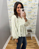 A woman takes a mirror selfie wearing a light green and white vertically striped blouse with a ruffled peplum hem, paired with dark blue jeans.