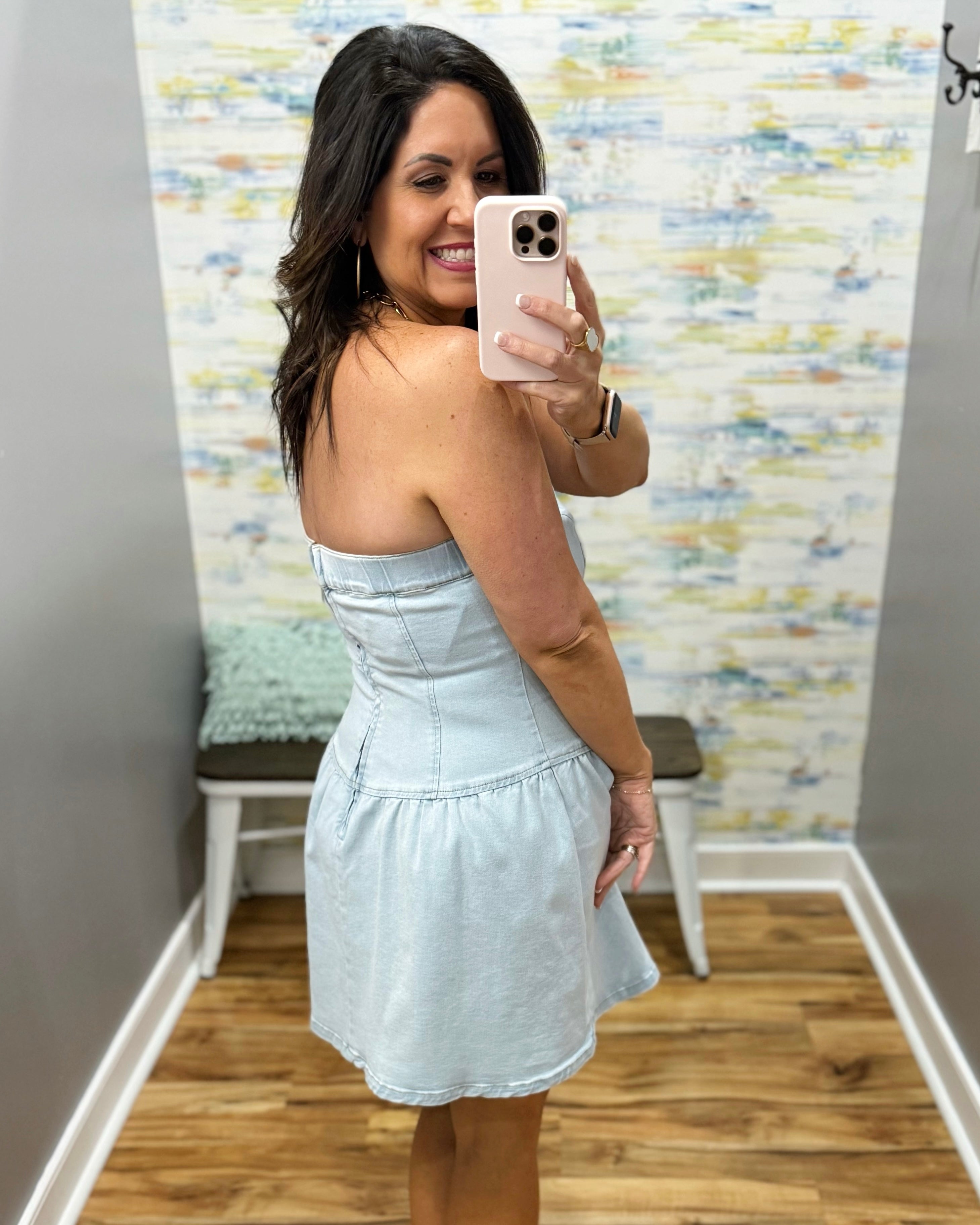 Woman taking a mirror selfie wearing a light blue dress in a room with a textured wall.