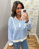 A woman takes a mirror selfie wearing a blue and white striped quarter-zip knit sweater with white trim, paired with blue jeans.
