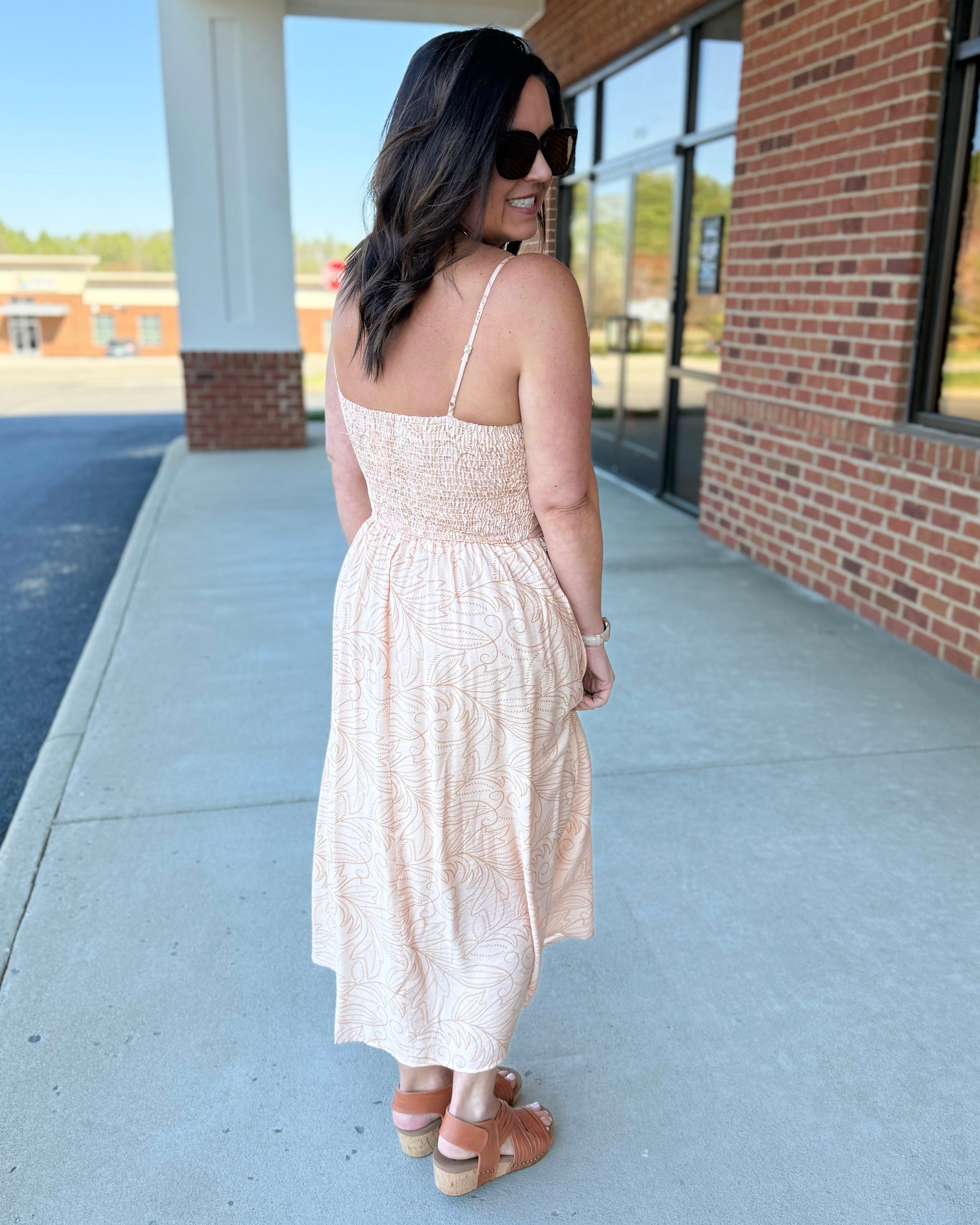 Woman in a beige dress standing on a sidewalk near a building.