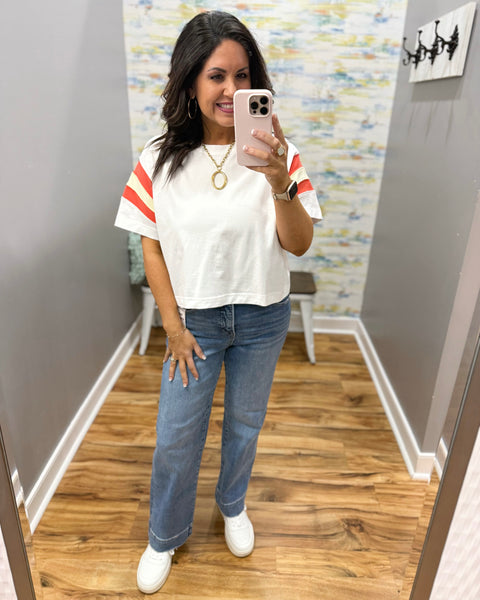 woman wearing white tee with colorful sleeves, chunky gold necklace, and risen straight jeans.