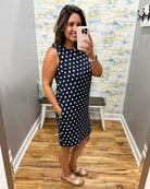 Woman taking a mirror selfie wearing a black polka dot dress in a fitting room.