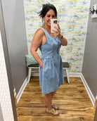 Woman taking a mirror selfie wearing a blue denim dress in a room with patterned wallpaper.