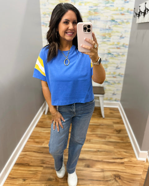 woman wearing blue tee with risen straight leg jeans, white sneakers, and chunky gold necklace