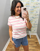 Woman taking a mirror selfie wearing a pink and white striped shirt and blue shorts.