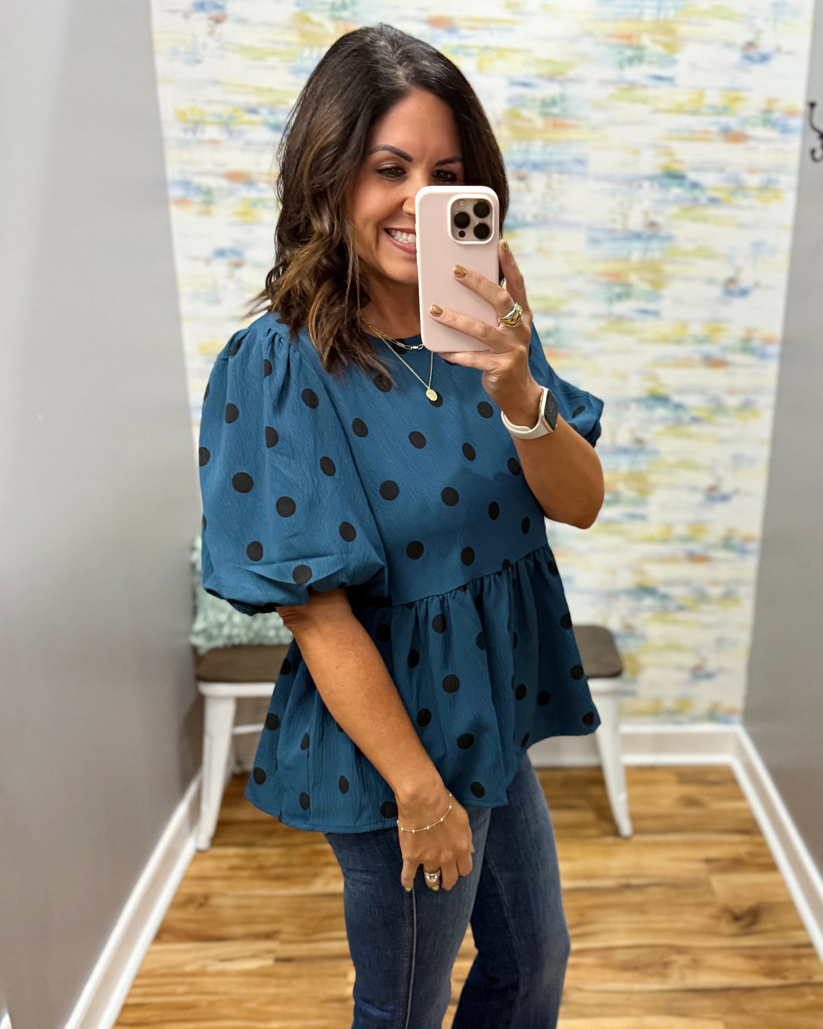 woman taking a selfie wearing a teal top with black polka dots and puff sleeves.