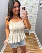 Woman taking a mirror selfie wearing a beige peplum top and denim shorts.