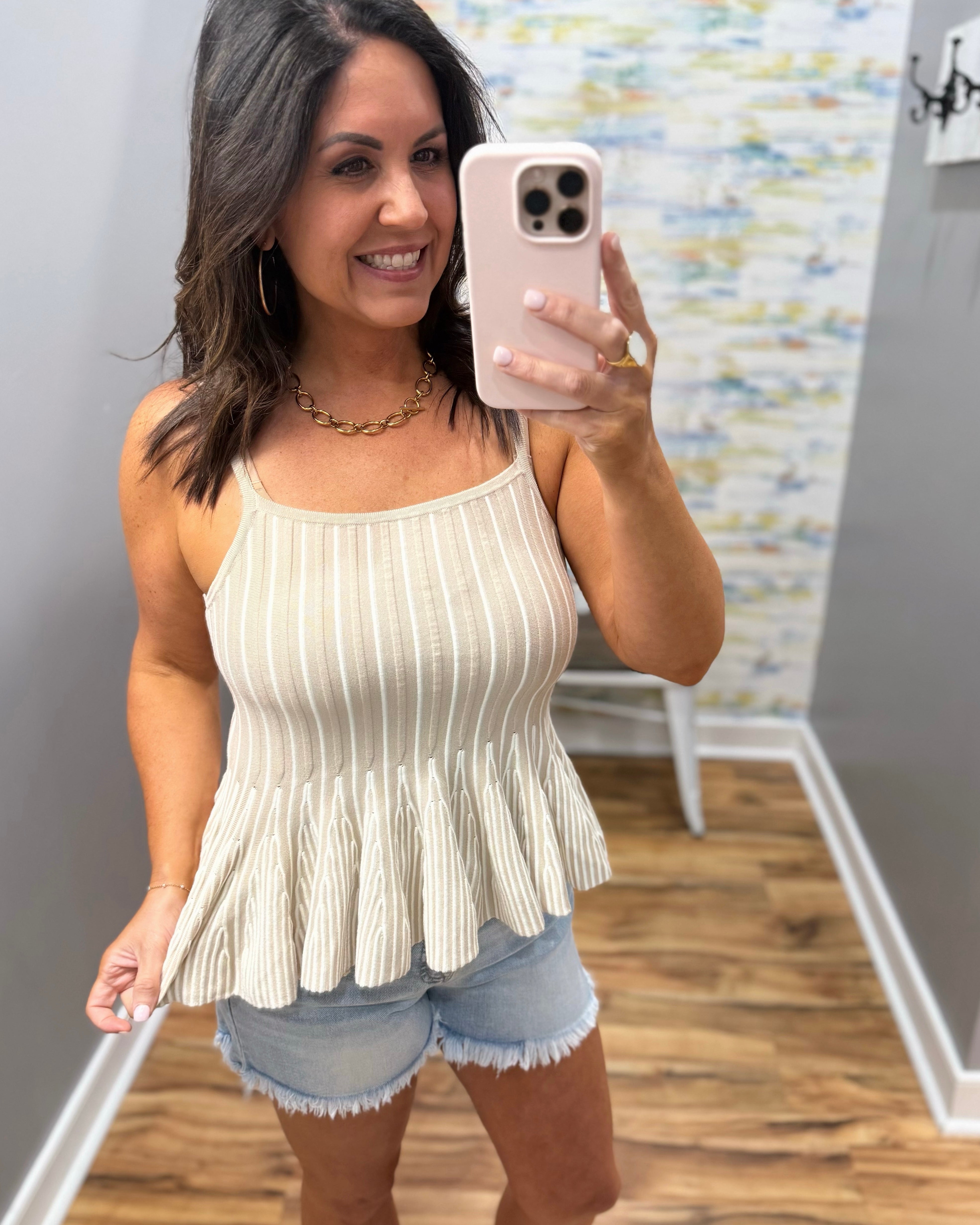 Woman taking a mirror selfie wearing a beige peplum top and denim shorts.
