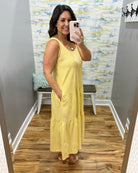 Woman wearing a yellow dress taking a mirror selfie in a room with a textured wall.