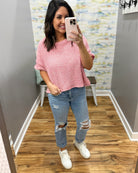 Woman taking a mirror selfie wearing a pink top and ripped jeans.