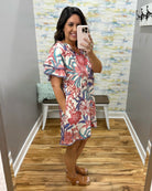 Woman taking a mirror selfie wearing a floral dress in a room with a colorful wall.