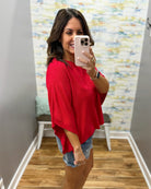 woman wearing a red dolman top and denim shorts.