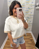 Woman taking a mirror selfie wearing a white top and denim shorts in a room with a colorful wall.