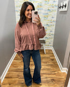 A woman takes a mirror selfie wearing a dusty rose long-sleeve ruffled blouse and dark blue flare jeans in a home hallway.