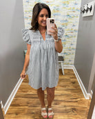 Woman taking a mirror selfie wearing a black and white striped dress in a room with wooden flooring and colorful wall.