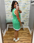 Woman taking a mirror selfie wearing a green dress in a room with a textured wall and wooden floor.