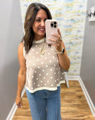 Woman taking a mirror selfie wearing a polka dot top and blue jeans.