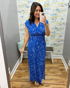 Woman taking a mirror selfie wearing a blue floral dress in a store.