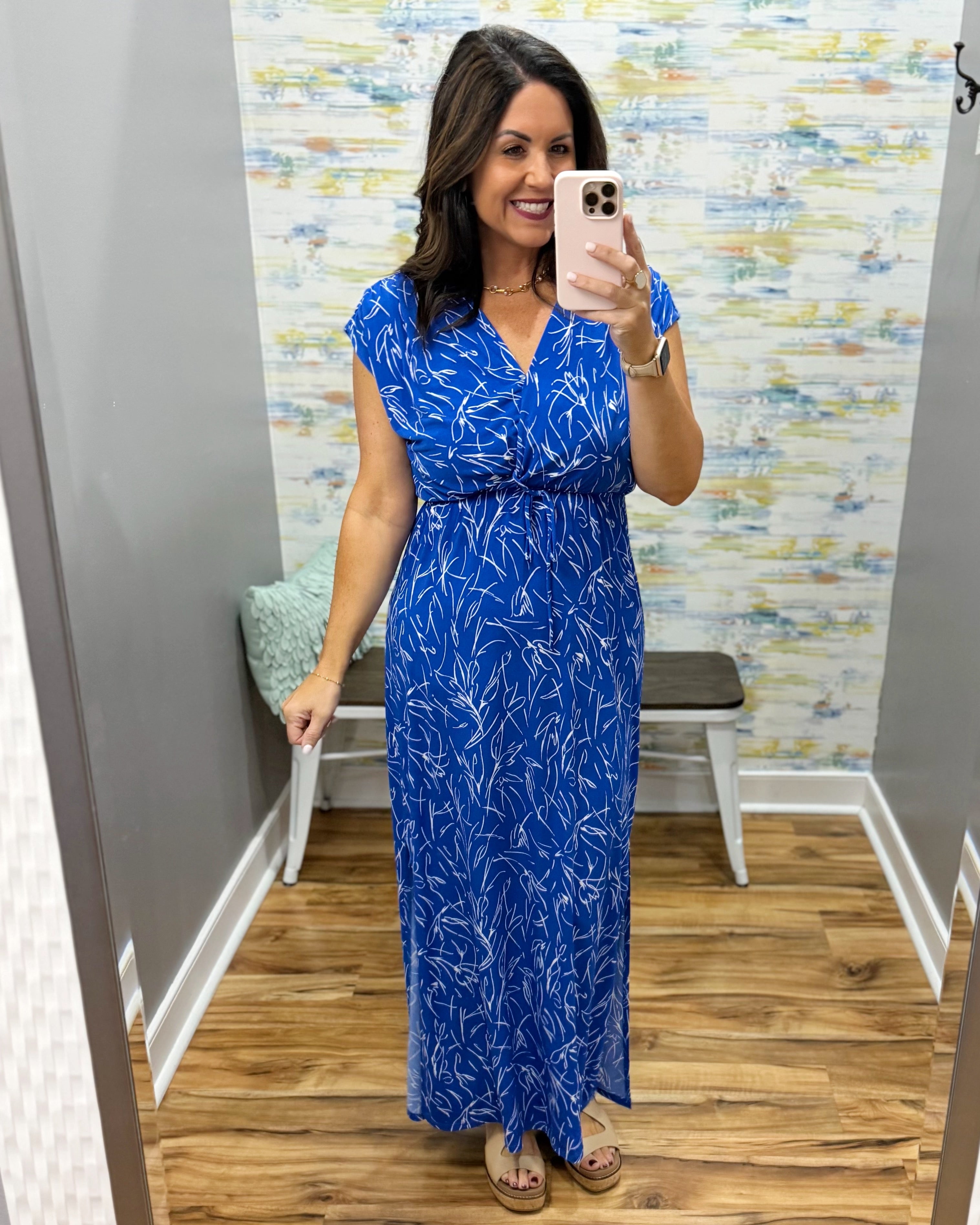 Woman taking a mirror selfie wearing a blue floral dress in a store.